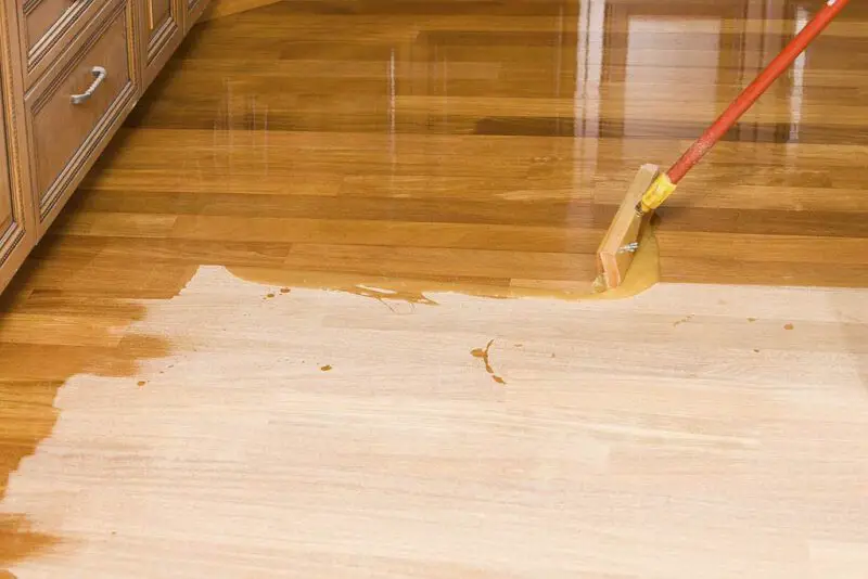 Applying polyurethane varnish in hardwood floor with long handle applicator