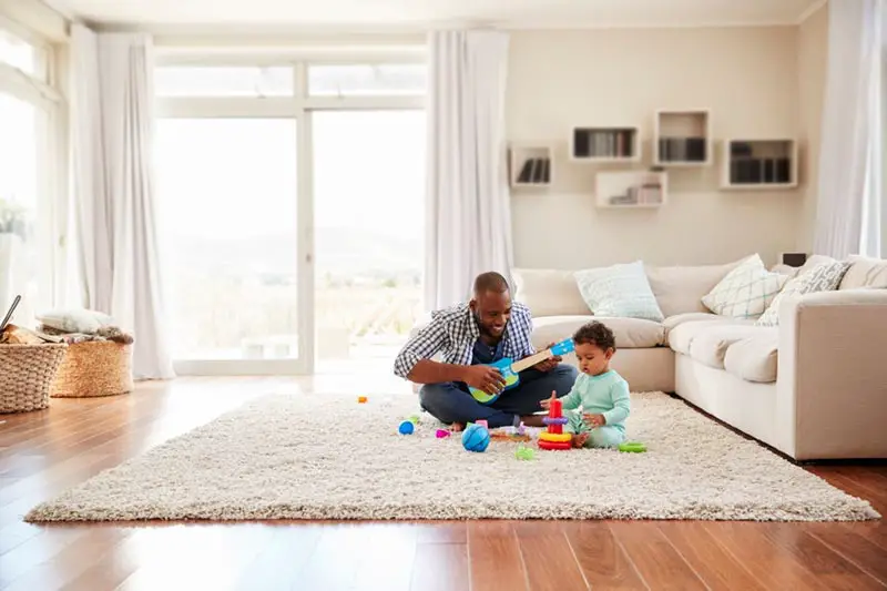 a black father and toddler playing in sitting room with area rug on wood floor